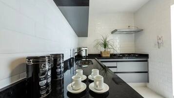 A modern kitchen with white subway tiles, black countertops, and stainless steel appliances. There are three coffee cans, four white cups, and a potted plant on the counter.