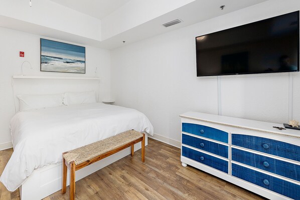 A bedroom with a bed, a bench, a dresser, a TV, and a painting on the wall. - Salt Air Villas #214 | Close to Beach | Pool & Gated Community (Saint Simons Island)