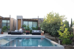 Ein moderner Poolbereich im Freien mit integriertem Sitzbereich und einer großen, verglasten Struktur im Hintergrund.