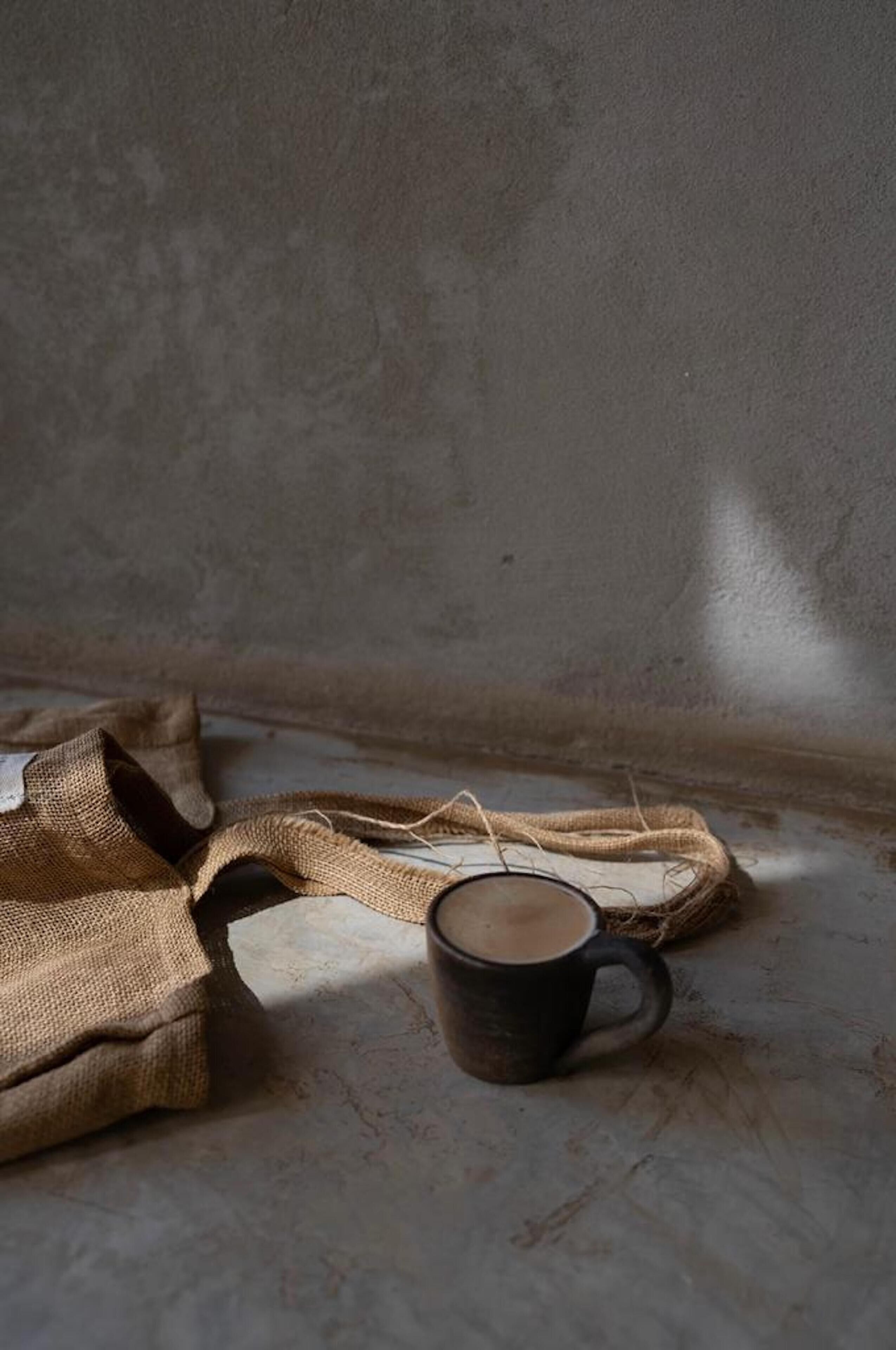 Ein Jutbeutel und eine dunkle Tasse mit einem Getränk auf einer strukturierten Oberfläche.