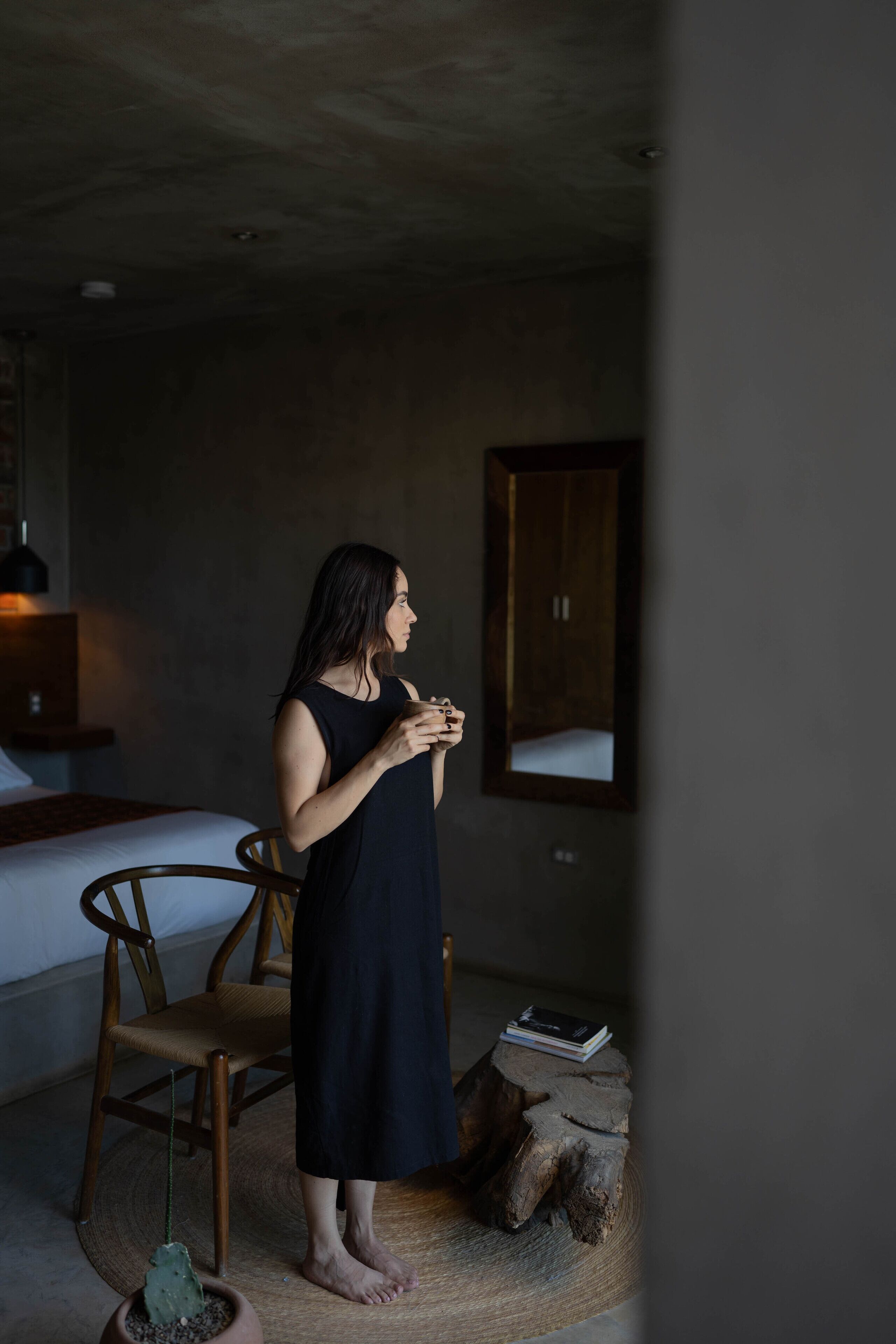 Una habitación con una cama, una silla, un taburete de madera y una planta en maceta.