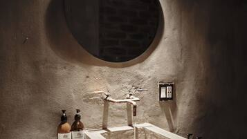 Un baño con un espejo redondo, un lavamanos y dos botellas de loción.