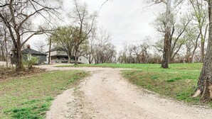 A rural dirt road leading to a house surrounded by trees.