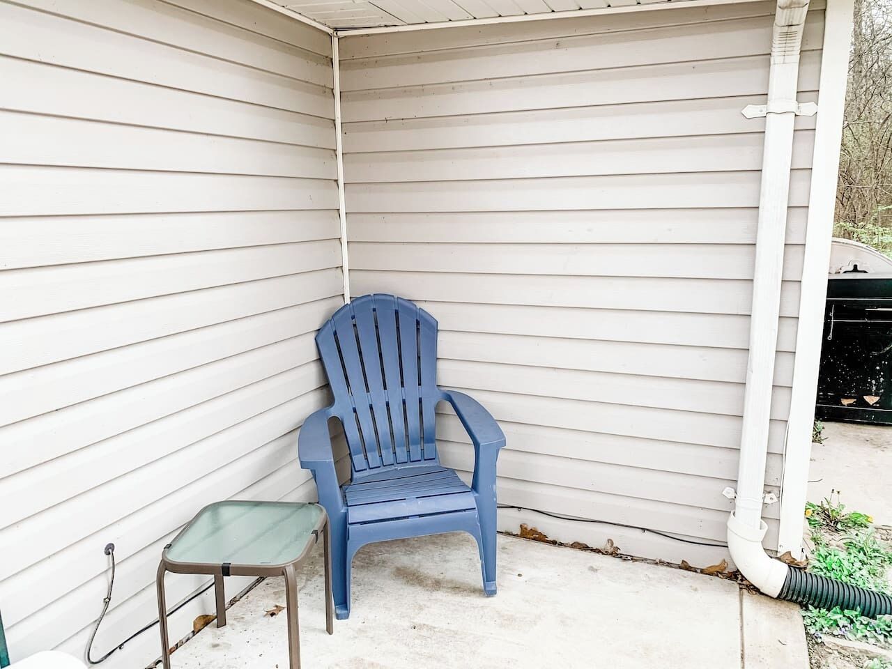 Esquina de una casa con una silla de plástico azul y una mesita.