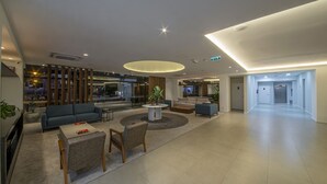 A spacious lobby with a modern design, featuring a central seating area with sofas and a coffee table, a reception desk, and a clear view of the entrance. - Laghetto Stilo Vita (Gramado)