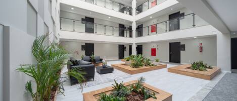 Un vaste atrium à plusieurs niveaux, agrémenté de jardinières en bois remplies de plantes, et un espace détente avec des canapés et une table basse.