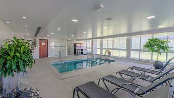 An indoor swimming pool with clear water, surrounded by lounge chairs and potted plants.