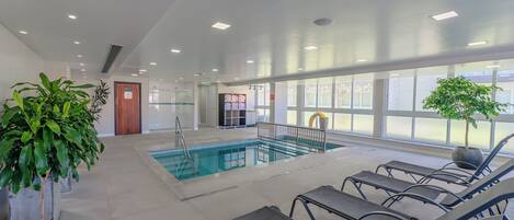 Una piscina interior con agua cristalina, rodeada de sillones de descanso y plantas en macetas.