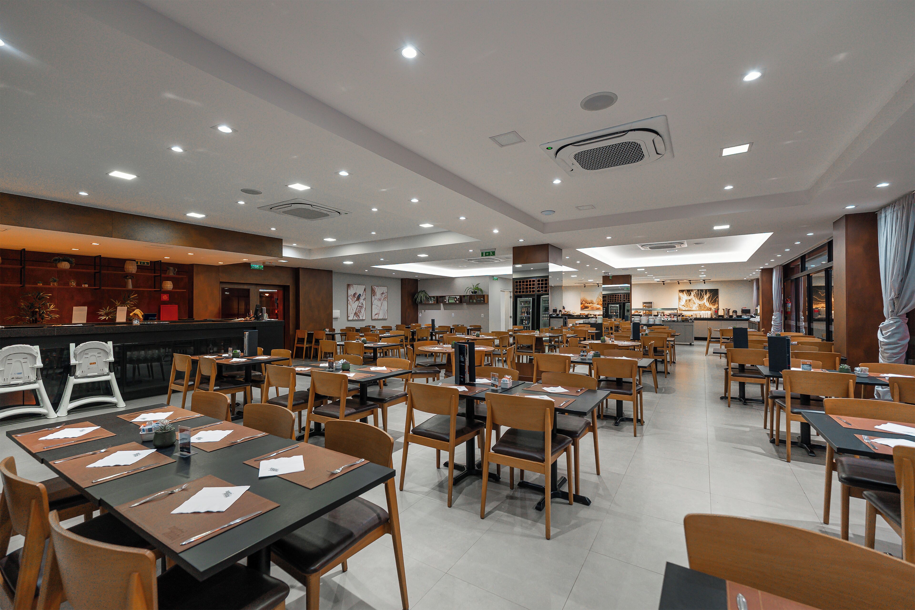 A spacious restaurant with multiple dining tables and chairs, a counter area, and a kitchen in the background.