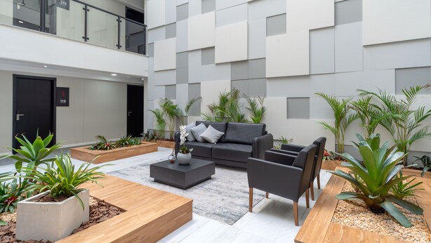 A modern indoor space with a grey sofa, wooden coffee table, and black chairs. There are potted plants and a marble floor. - Laghetto Stilo Vita (Gramado)