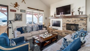 A spacious living room with a stone fireplace, a large flat-screen TV mounted above it, and a cozy seating area with a sofa and armchairs. - Gorgeous 5 bedroom 4.5 bath home with incredible mountain and lake views. (Eden)