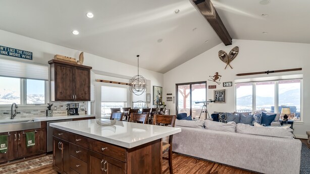 A modern kitchen with a large island, wooden cabinets, and a dining area with a view. - Gorgeous 5 bedroom 4.5 bath home with incredible mountain and lake views. (Eden)