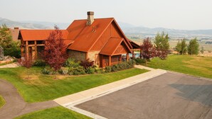A large, rustic-style house with a prominent chimney, surrounded by a well-maintained lawn and a paved driveway. - Gorgeous 5 bedroom 4.5 bath home with incredible mountain and lake views. (Eden)