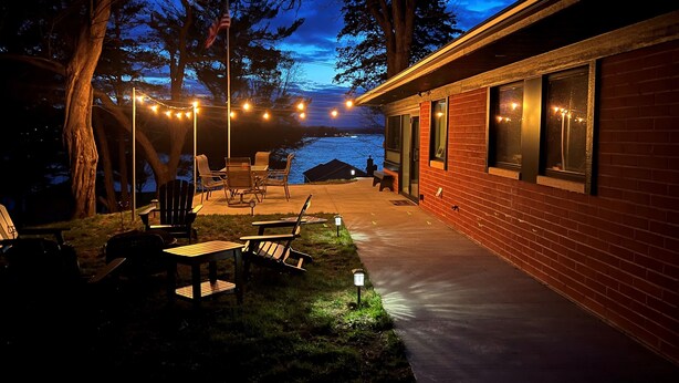 Une terrasse extérieure agrémentée de guirlandes lumineuses, de chaises et d’une table.