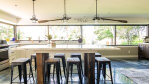 Une cuisine spacieuse dotée d’un grand îlot central, de tabourets de bar et d’un ventilateur de plafond.