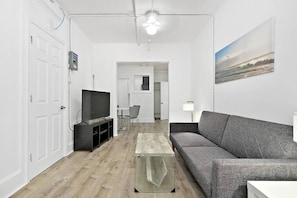 Una sala de estar moderna con un sofá gris, una mesa de centro de vidrio, un televisor de pantalla plana y un cuadro en la pared.