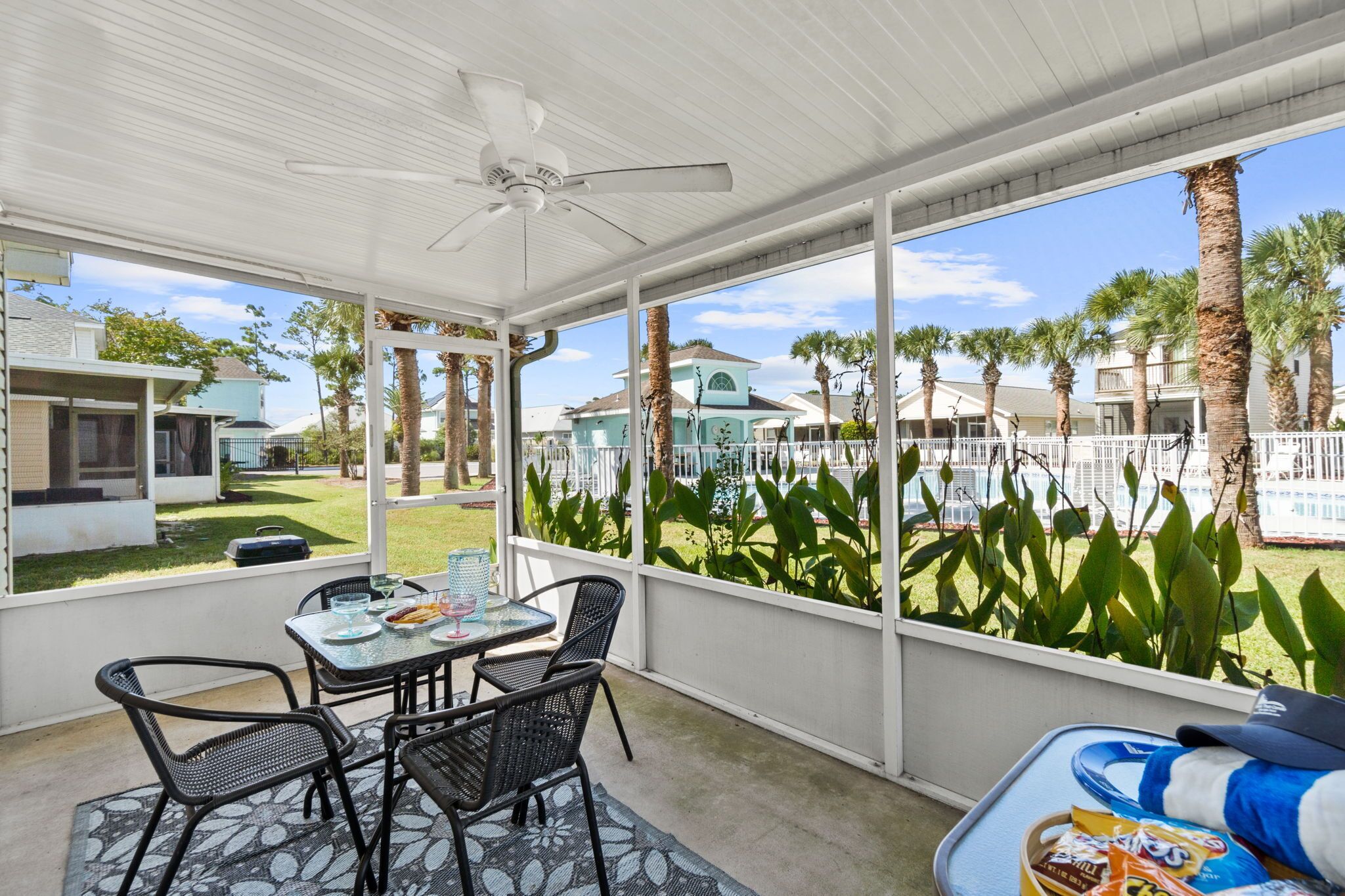 A covered patio with a table and chairs, a ceiling fan, and a view of a residential area with palm trees and houses.