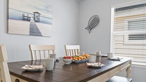 A dining area with a wooden table, white chairs, and a view of the ocean through a window.