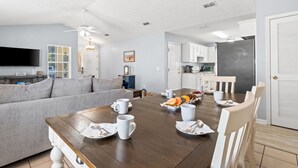 A modern living room with a dining table set for breakfast, a grey sofa, and a kitchen in the background.