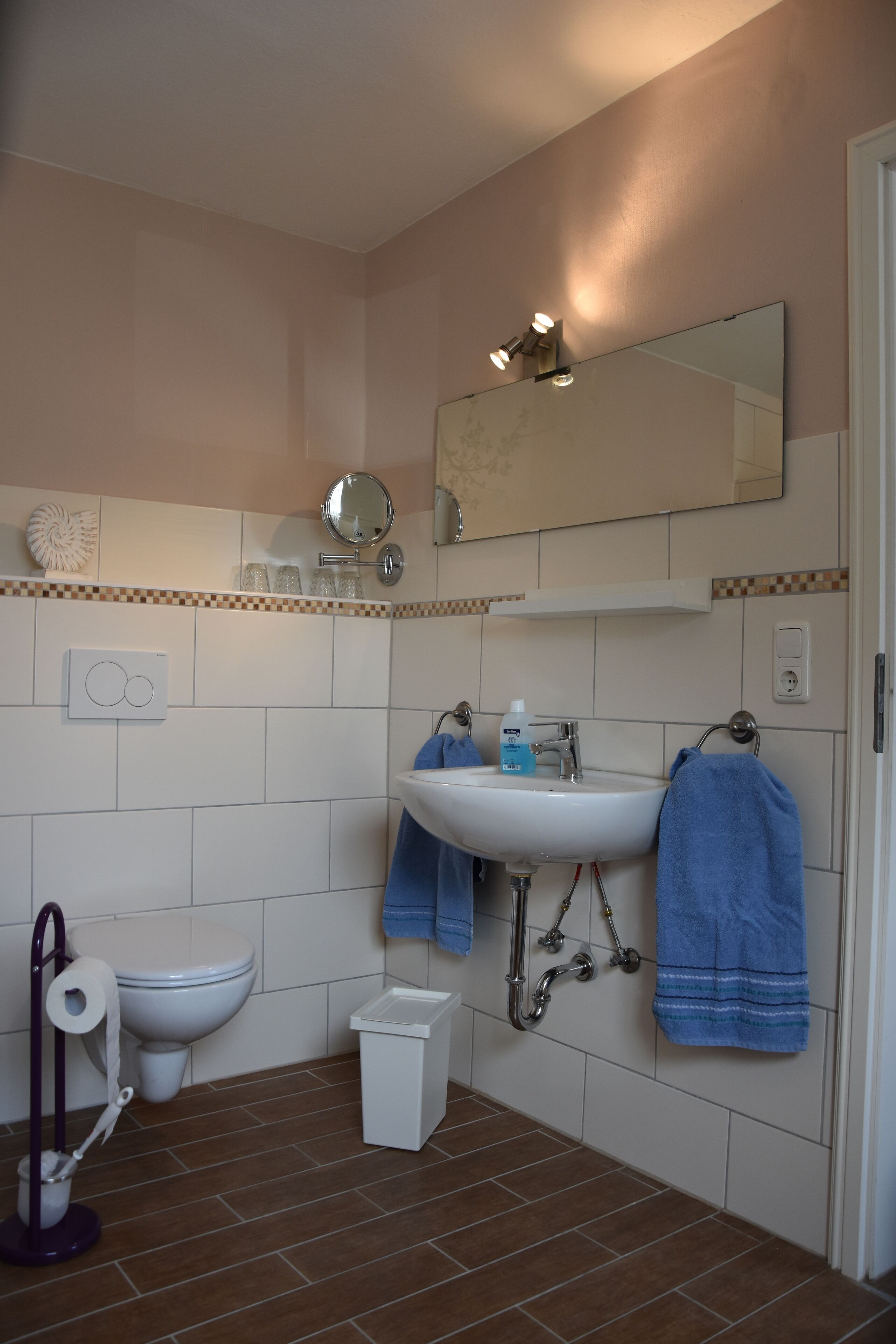 Une salle de bain avec un lavabo blanc, un miroir, des toilettes et une poubelle.