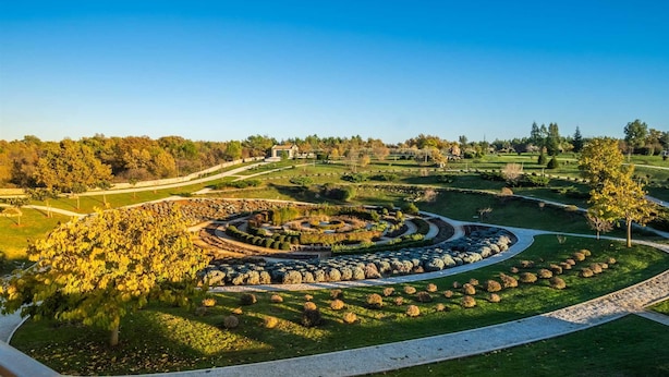 En vackert anlagd park med en cirkelformad stenformation, gångvägar och ett stort utbud av träd och buskar.