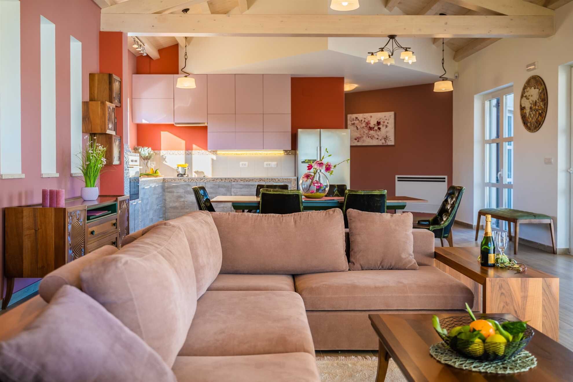 Una sala moderna con un sofá seccional, un comedor con una mesa y sillas, y una cocina al fondo.