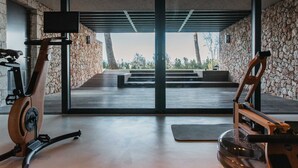 Une salle de sport moderne équipée de vélos d’appartement, dotée d’une grande fenêtre et d’un mur en pierre.
