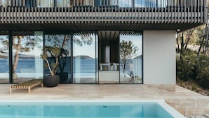 Une maison moderne dotée d’une grande baie vitrée donnant sur un lac, une piscine et une terrasse en bois.