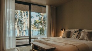Camera da letto con un letto grande, una panca e vista su alberi attraverso una porta-finestra in vetro.