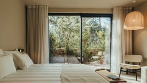 Una camera da letto con un letto grande, una sedia, un tavolo e vista su un giardino tramite una porta scorrevole.