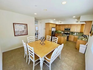 Una cocina compacta con armarios de madera, una isla central y un comedor con mesa de madera y sillas blancas.