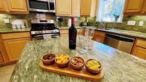 A kitchen with wooden cabinets, a granite countertop, a microwave, a stove, and a wine bottle.