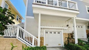 A two-story house with a white garage door, a balcony with white railings, and a stone wall with climbing plants.