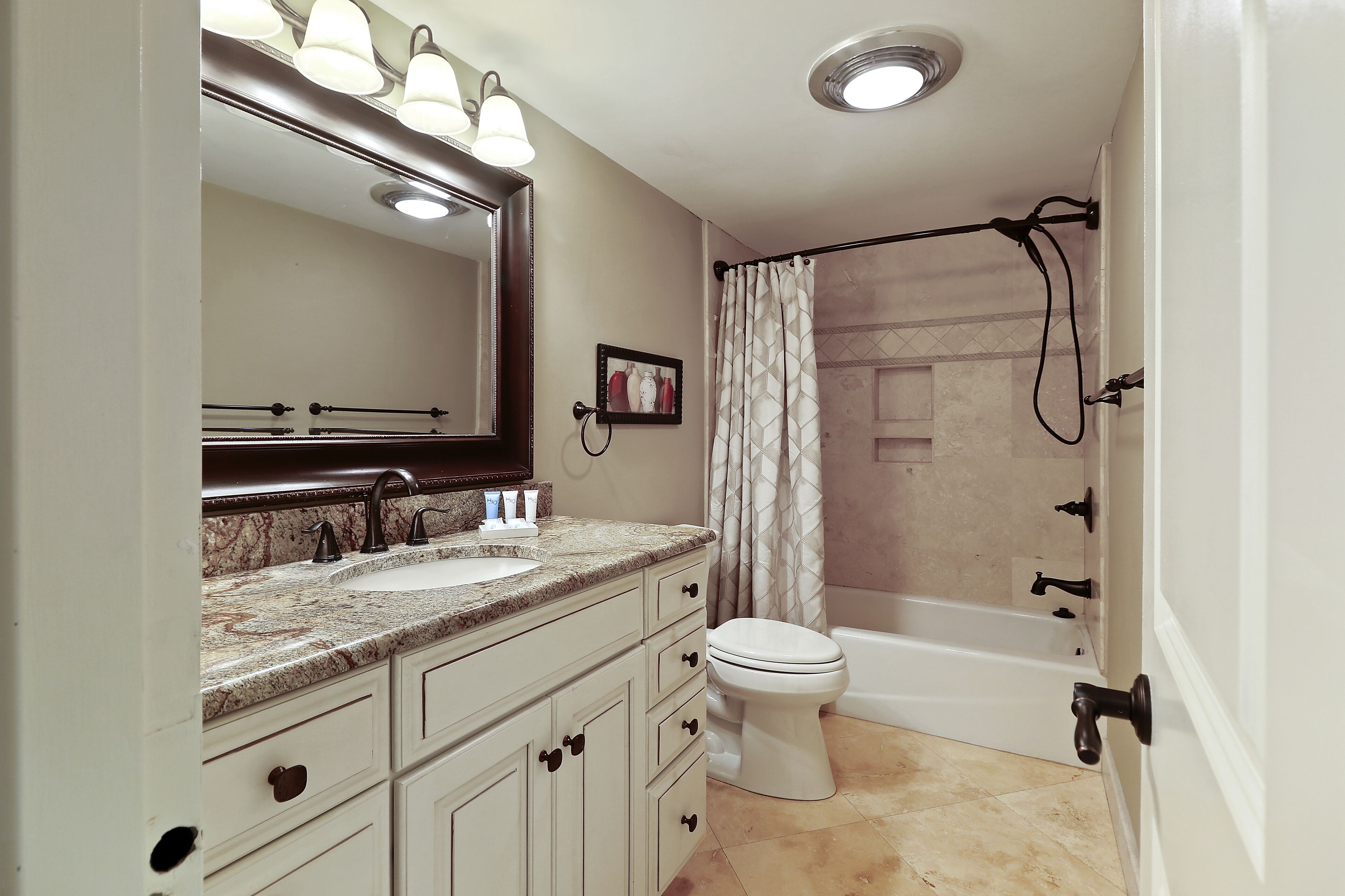 A bathroom with a sink, mirror, toilet, and shower area.