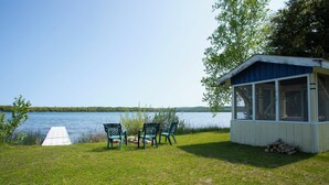 Un chalet au bord du lac, avec un quai, des chaises et un petit abri de jardin.