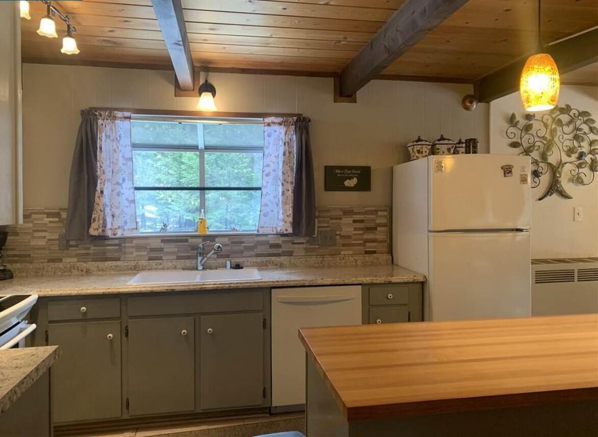 A kitchen with a wooden ceiling, a window with curtains, a refrigerator, and a sink.