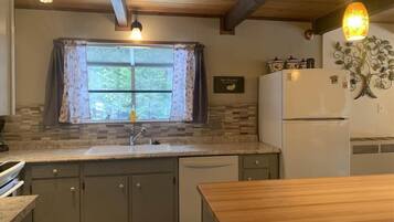 A kitchen with a wooden ceiling, a window with curtains, a refrigerator, and a sink.