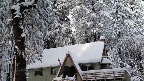 A cabin with a steep roof, surrounded by snow-covered trees. - 4 bdrm 2 bath - sleeps 10 living & family room space for everyone! Dogs okay. (Arnold)
