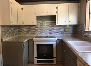 Kitchen features an oven, sink, and mosaic-tiled backsplash.