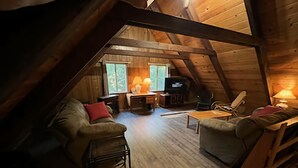 An attic-style room with wooden beams, a sofa, a chair, a table, and a TV. - 4 bdrm 2 bath - sleeps 10 living & family room space for everyone! Dogs okay. (Arnold)