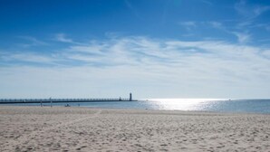 Una platja amb un moll que s'endinsa a l'aigua, un far i un cel serè.