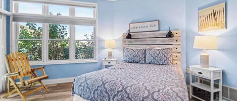 Une chambre à coucher avec un grand lit, une chaise en bois, une table de chevet et une lampe fixée au mur.