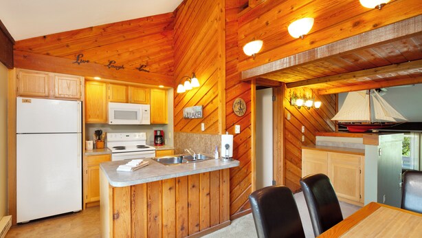 Una cocina con paredes de madera, un refrigerador blanco, un microondas, una estufa y un lavamanos. Hay una mesa de comedor con sillas y una decoración náutica de un velero en la pared.