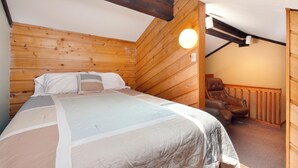 Una habitación de madera con cama, una silla y techo inclinado.