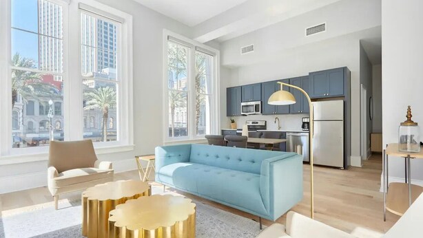Una sala de estar moderna con un sofá azul, un sillón beige y una mesa de centro dorada.