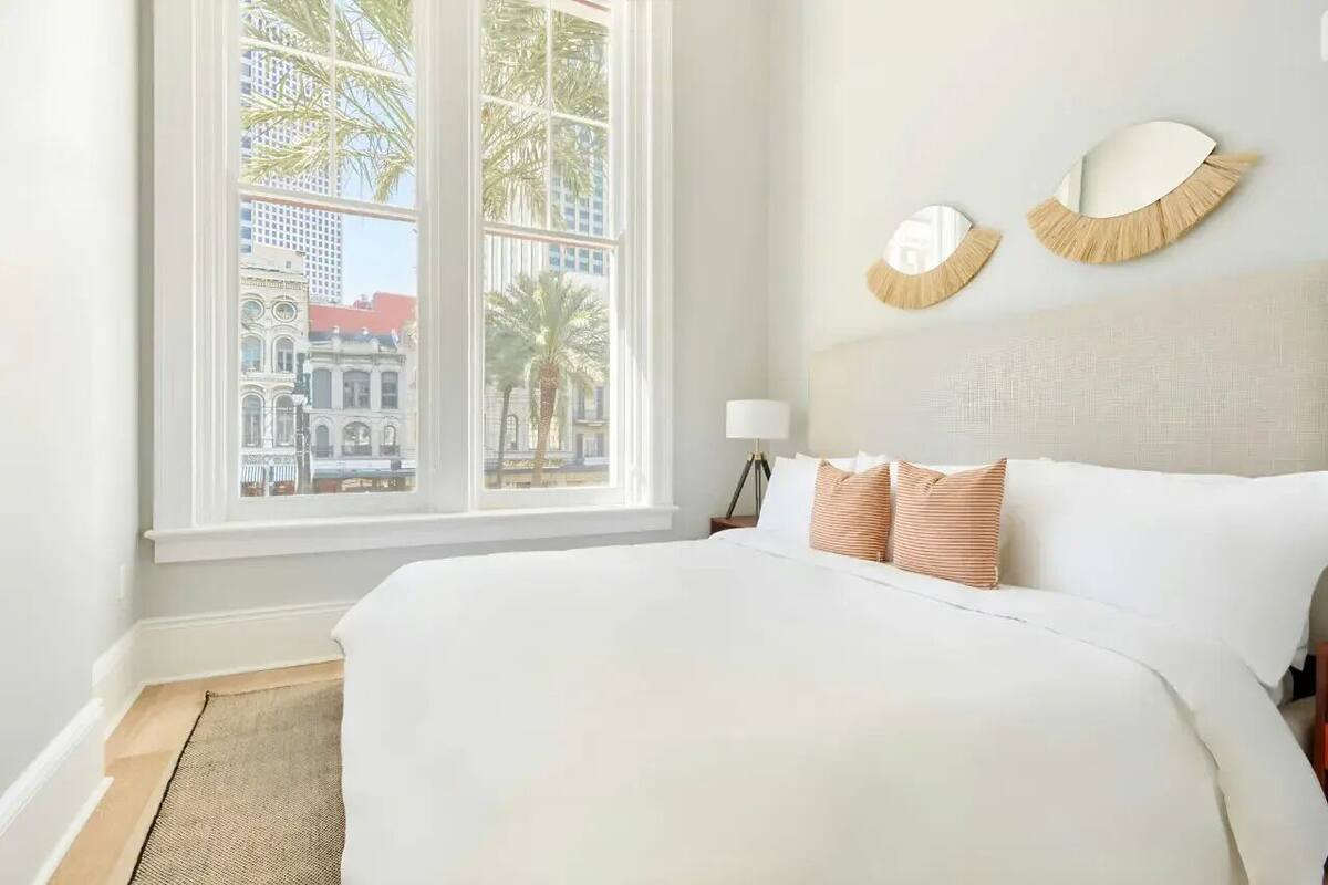 A hotel room with a large bed, a view of palm trees and buildings, and two wall-mounted mirrors.