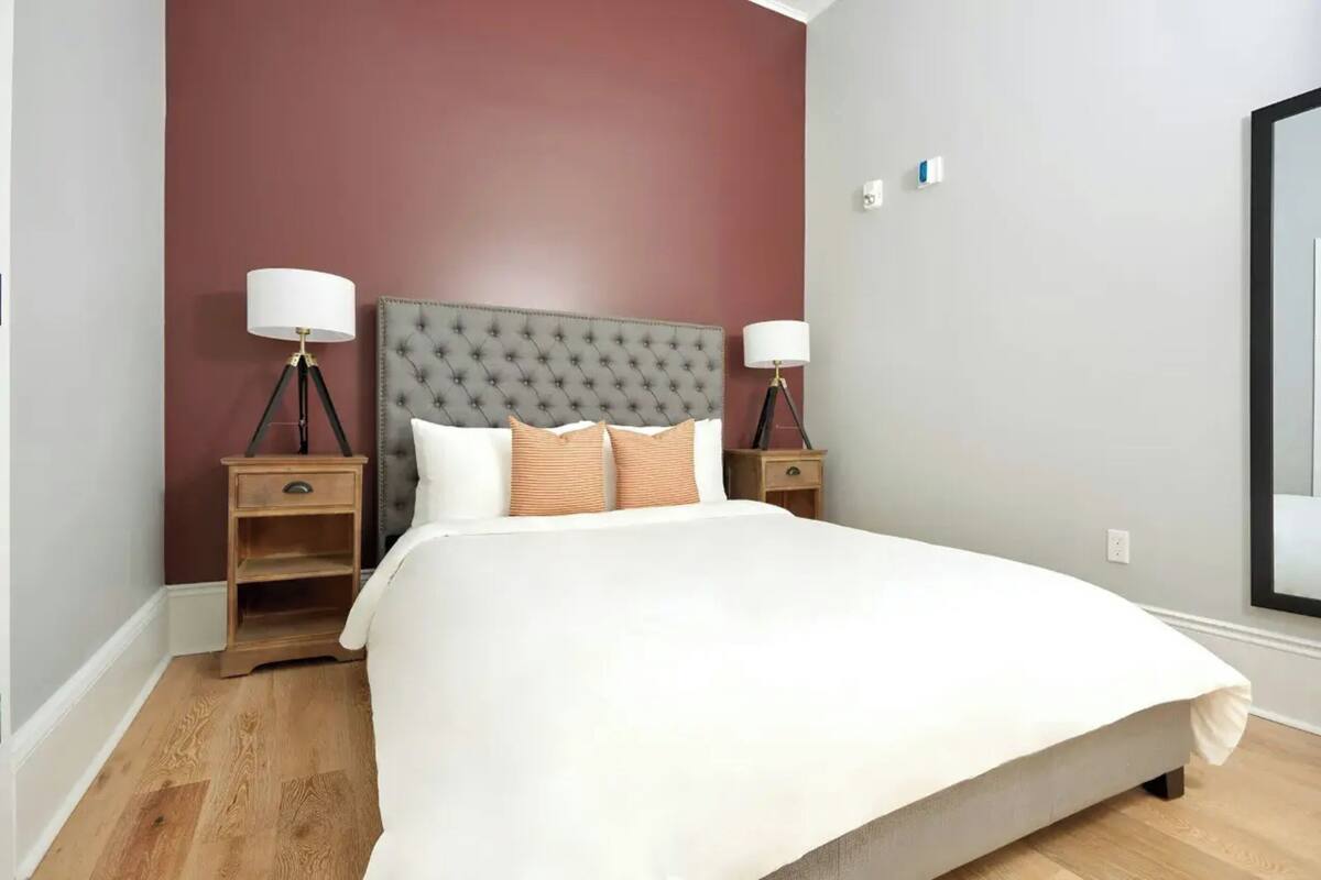 A bedroom with a tufted headboard, a large bed, two bedside tables with lamps, and a wooden floor.