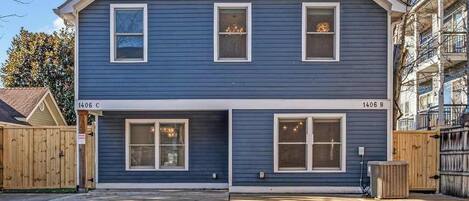 A two-story residential building with a dark blue exterior, numbered 1406 C and 1406 B, featuring large windows and a visible air conditioning unit.