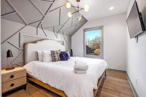 A modern bedroom with a geometric ceiling design, a large bed with white bedding, a nightstand, and a TV mounted on the wall. - Private Downtown Luxury Retreat - Hot Tub (Nashville)