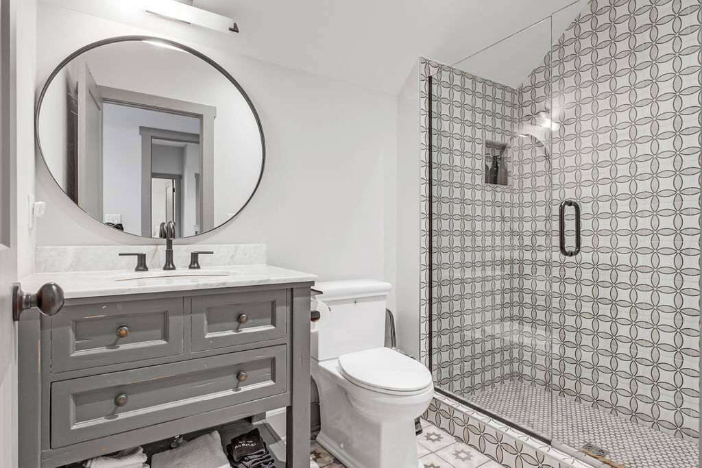 A bathroom with a round mirror, a toilet, and a shower with patterned tiles.